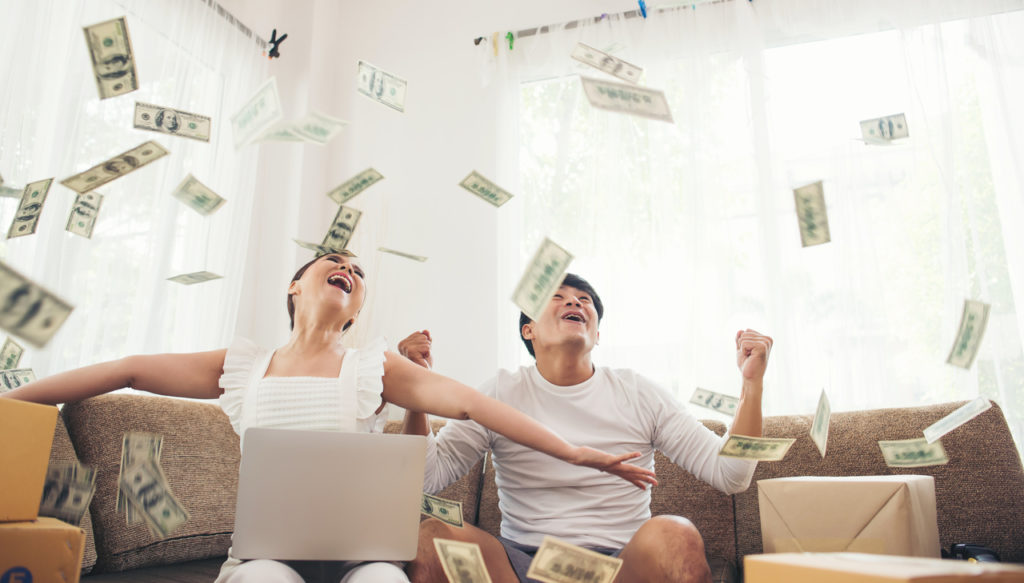 Happy couple smiling successful sitting under money rain. Business online concept