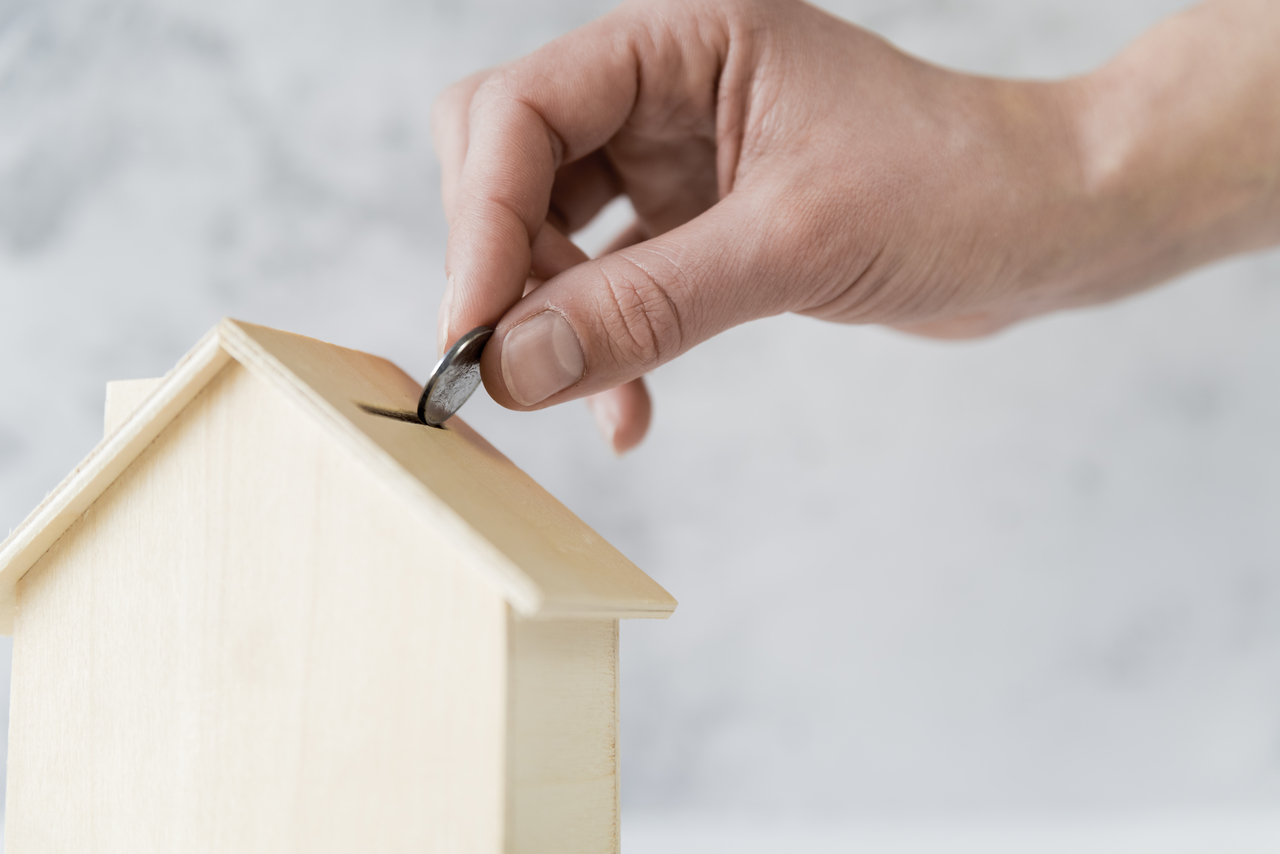 hand inserting coin into coin bank shaped like house